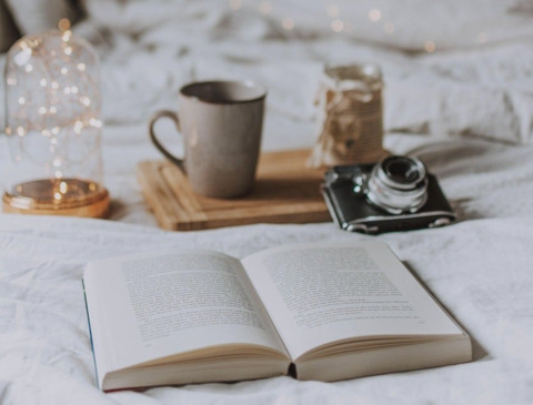 a woman sitting in a chair reading a book with a cup of coffee next to her and a set of eye glasses