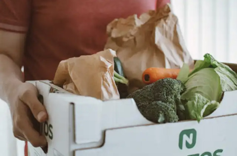A person holding a box of fresh produce likely from a co-op or farmers market
