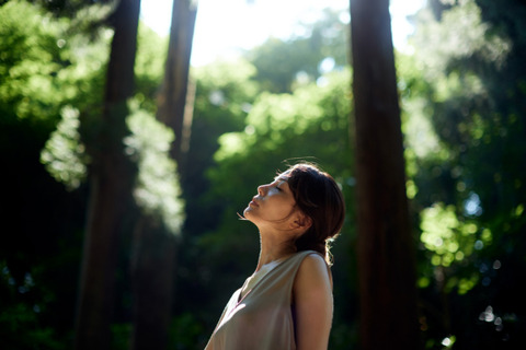 a woman is in a forest and is taking a deep breath