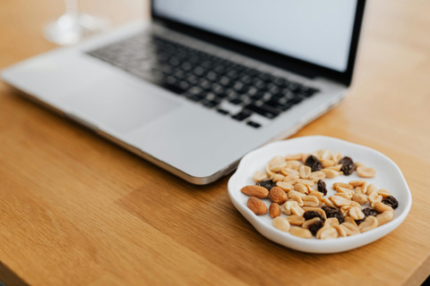 a bowl of nuts and dried fruit are on a table next to a laptop