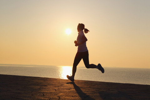 A woman is running in front of the ocean as the sun rises