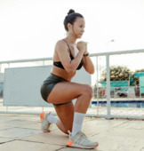 Woman in a black shorts and tank top. She is in a lunge position with one knee on the ground.