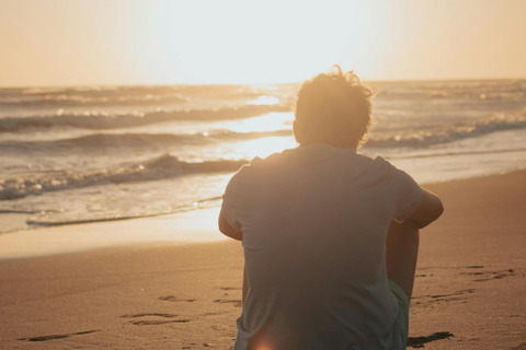 A man is sitting on the beach watching the sunset