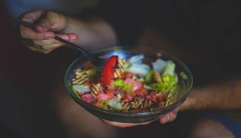 A person is eating a bowl of pasta and vegetables with a fork