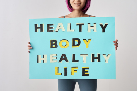 a woman is holding up a sign that says "Healthy Body, Healthy Life"