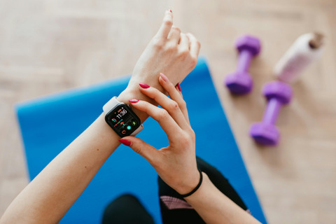 A woman is checking her workout on her smartwatch. there are dumbells, a water bottle and a yoga mat on the floor under her