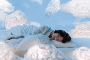 A woman in white pajamas is asleep and there are clouds all around her