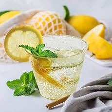 There are 2 glasses of water with slices of lemon, mint, and ice on a table