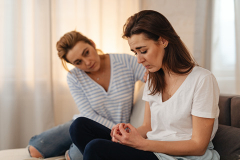 Two women sitting next to each other. One seems to be in distress and the other is comforting her