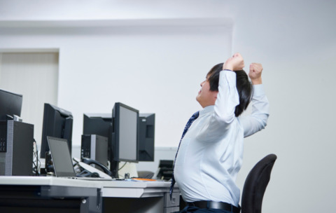 Woman in a white sweater sitting on an exercise ball while at a desk. 