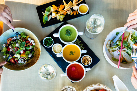 an overhead view of 2 people at a table. each has a different salad in front of them and there is a plate of sauces and another of cheese. 
